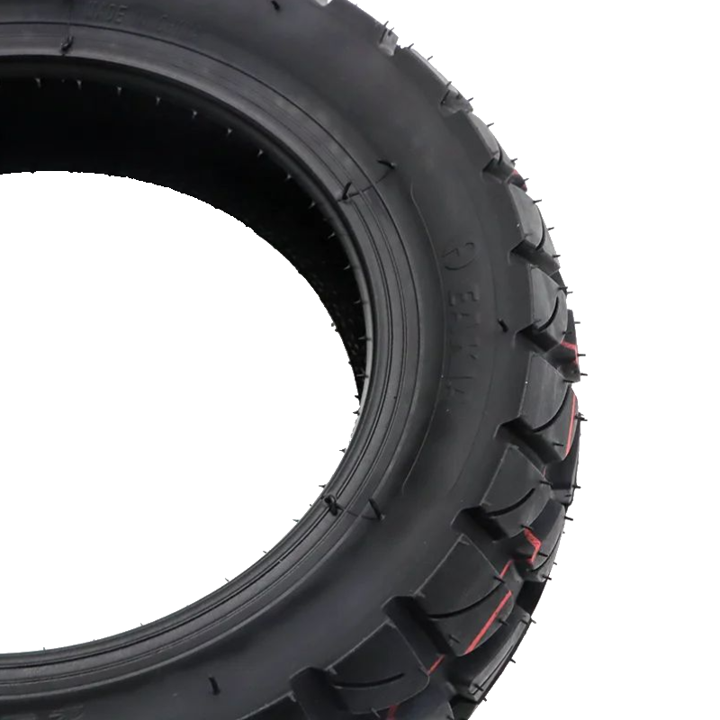 A close-up studio shot of a black rubber tire with deep tread blocks and small red accent lines, isolated on a white background.