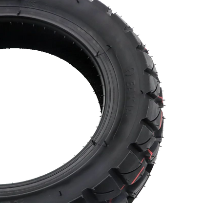 A close-up studio shot of a black rubber tire with deep tread blocks and small red accent lines, isolated on a white background.